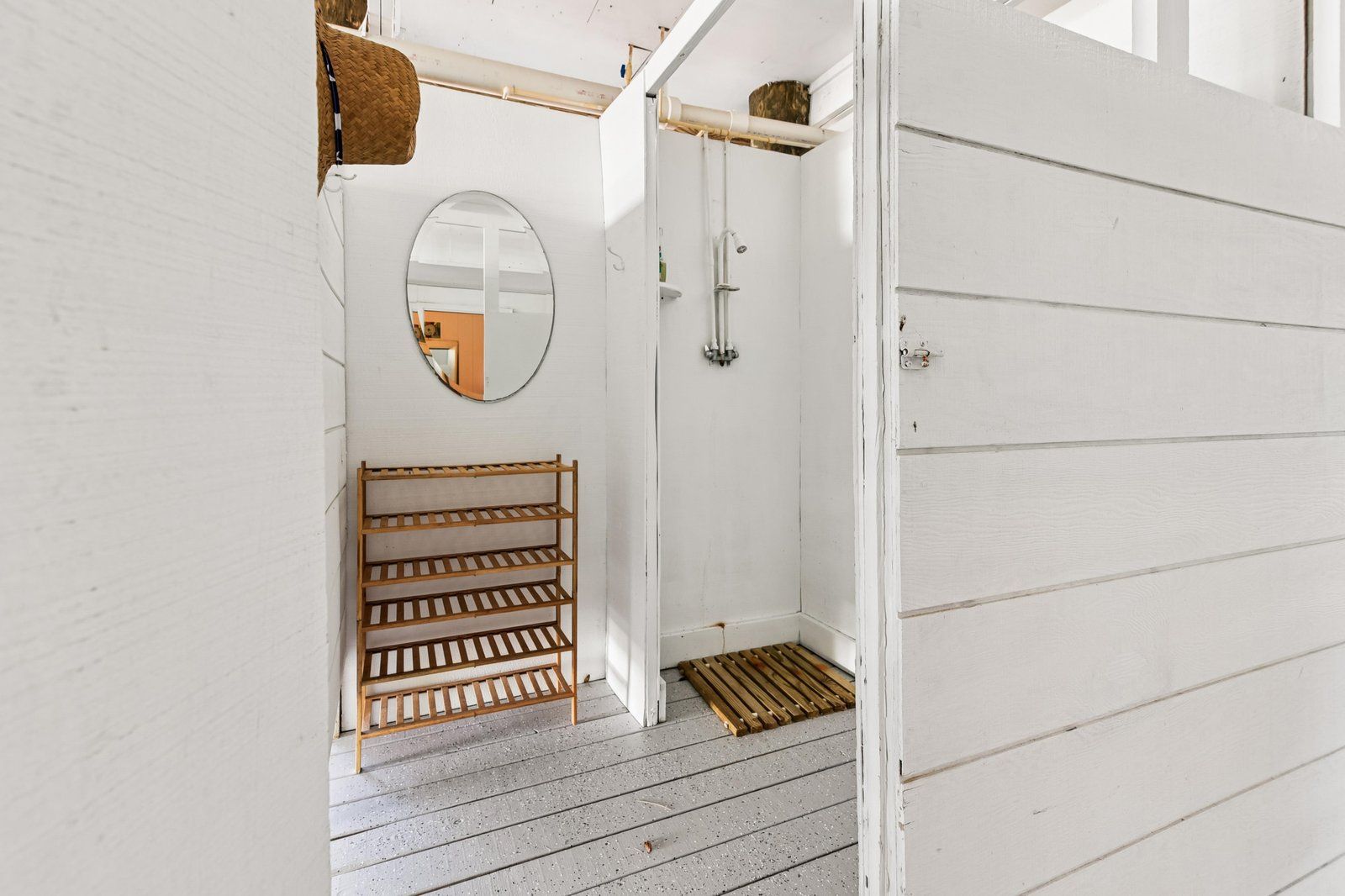A white wooden room with a wooden shelf, a mirror, and a shower area.