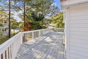 A wooden deck with white railings, surrounded by trees and a building. - Charming Oceanside Getaway! (Bethany Beach)