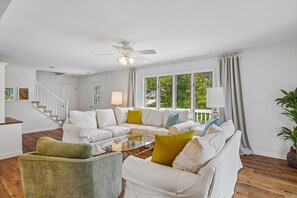 A spacious living room with a white sofa set, a green armchair, a glass coffee table, and a ceiling fan. - Charming Oceanside Getaway! (Bethany Beach)