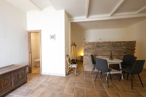 Une pièce avec un mur en pierre, un banc en bois, une table à manger avec des chaises et un fauteuil suspendu.