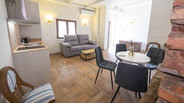 Ein kompakter Wohnraum mit Küchenzeile, einer Couch, einem Esstisch mit Stühlen und einer Wand aus Ziegelsteinen.
