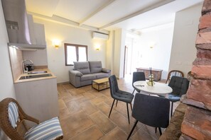 Ein kompakter Wohnraum mit Küchenzeile, einer Couch, einem Esstisch mit Stühlen und einer Wand aus Ziegelsteinen.
