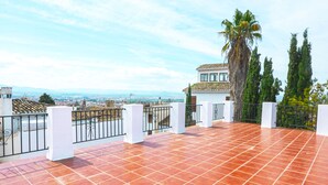 Eine Terrasse mit roten Fliesen, weißen Säulen und Blick auf die Stadt.