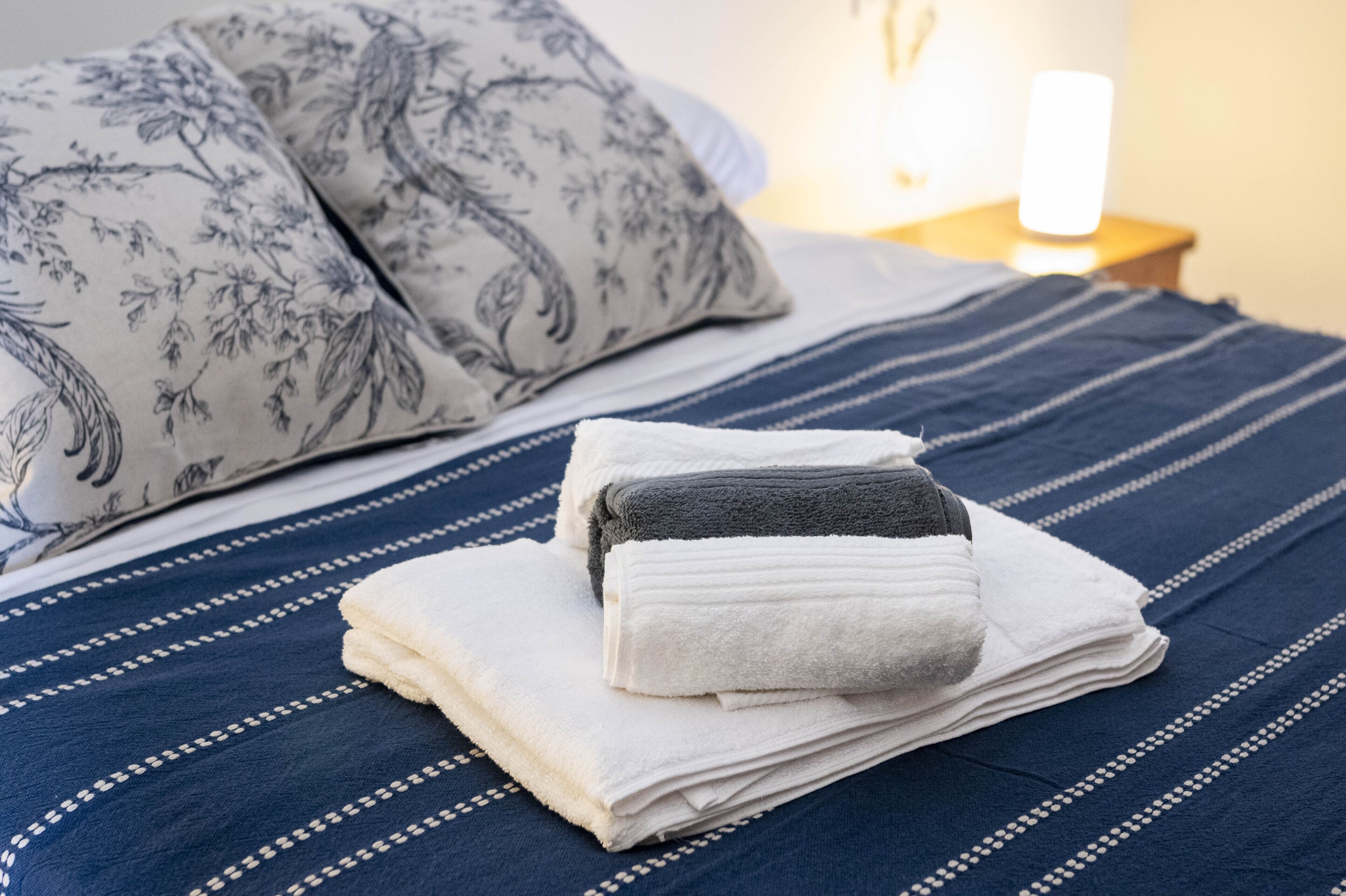 Ein ordentlich bezogenes Bett mit einer blau gestreiften Tagesdecke und einem Stapel gefalteter Handtücher.