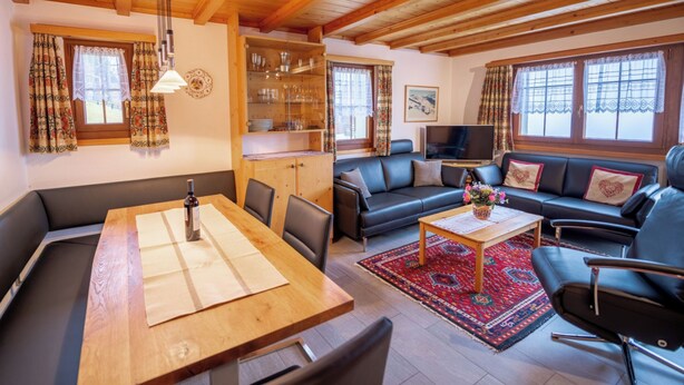 Una sala de estar acogedora con techo de madera, un comedor con mesa y sillas, un conjunto de sofás y un televisor.