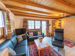 Ein Wohnzimmer mit Holzboden, einer Couch, einem Sessel, einem Fernseher und einem Bücherregal.