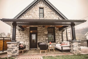 A stone house with a covered porch, a door, and two seating areas.