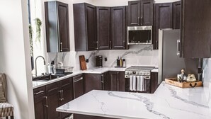 Una cocina moderna con gabinetes oscuros, una isla de mármol y dos taburetes de bar.