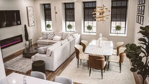 Una sala de estar moderna con sofá, mesa de comedor y sillas, chimenea y ventanas amplias.