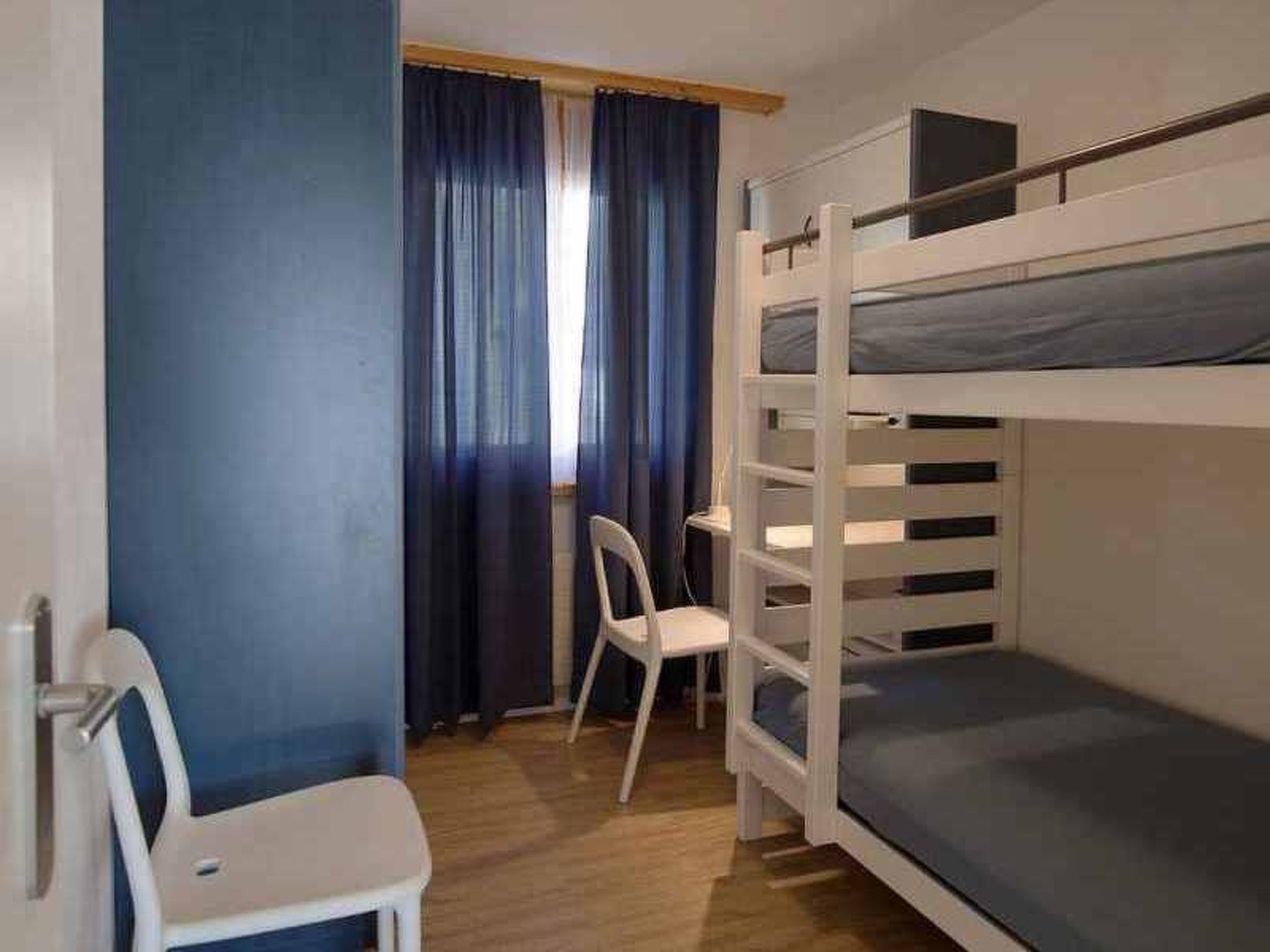 Ein Schlafraum mit Etagenbett, Schreibtisch und Stuhl, einem Fenster mit Vorhängen und Holzboden.