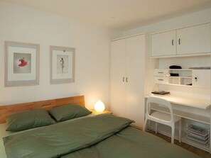 Un dormitorio con una cama, un escritorio con cajones y dos cuadros en la pared.