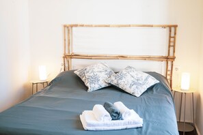 Ein Bett mit Bambus-Kopfteil, zwei gemusterte Kissen und gefaltete Handtücher.