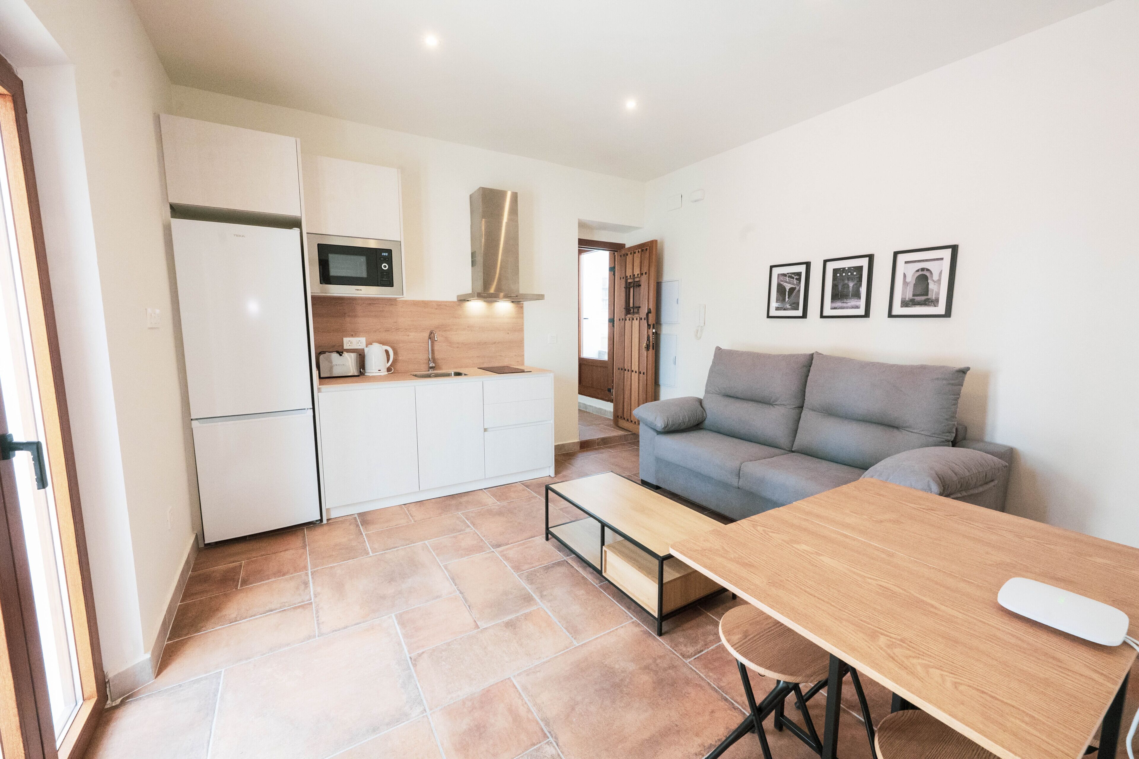 Une cuisine compacte équipée d’un four à micro-ondes, d’une cuisinière et de placards, ainsi qu’un canapé gris, une table en bois et une petite table basse.