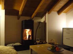 A cozy room with a fireplace, a table with a glass of wine, and a fruit bowl. - Signina Brun, Lumbrein, (Lumbrein), 48007B by Interhome (Lumbrein)