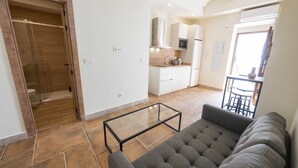 A modern living room with a sofa, a glass coffee table, and a kitchen area with cabinets and a microwave. - San Miguel Bajo Apartment (Granada)