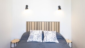 A neatly made bed with a dark bedspread, two patterned pillows, and folded towels. There are two bedside tables with lamps on either side of the bed. - San Miguel Bajo Apartment (Granada)