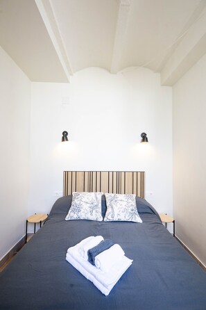 A neatly made bed with a dark bedspread, two patterned pillows, and folded towels. There are two bedside tables with lamps on either side of the bed. - San Miguel Bajo Apartment (Granada)