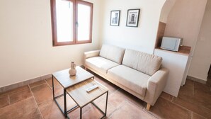 A living room with a sofa, a coffee table, a TV, and a window. - Torre de la Vela Apartment (Granada)