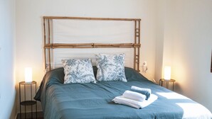 A neatly made bed with a green bedspread, two patterned pillows, and a stack of folded white towels. There are two bedside lamps on either side of the bed. - Torre de la Vela Apartment (Granada)