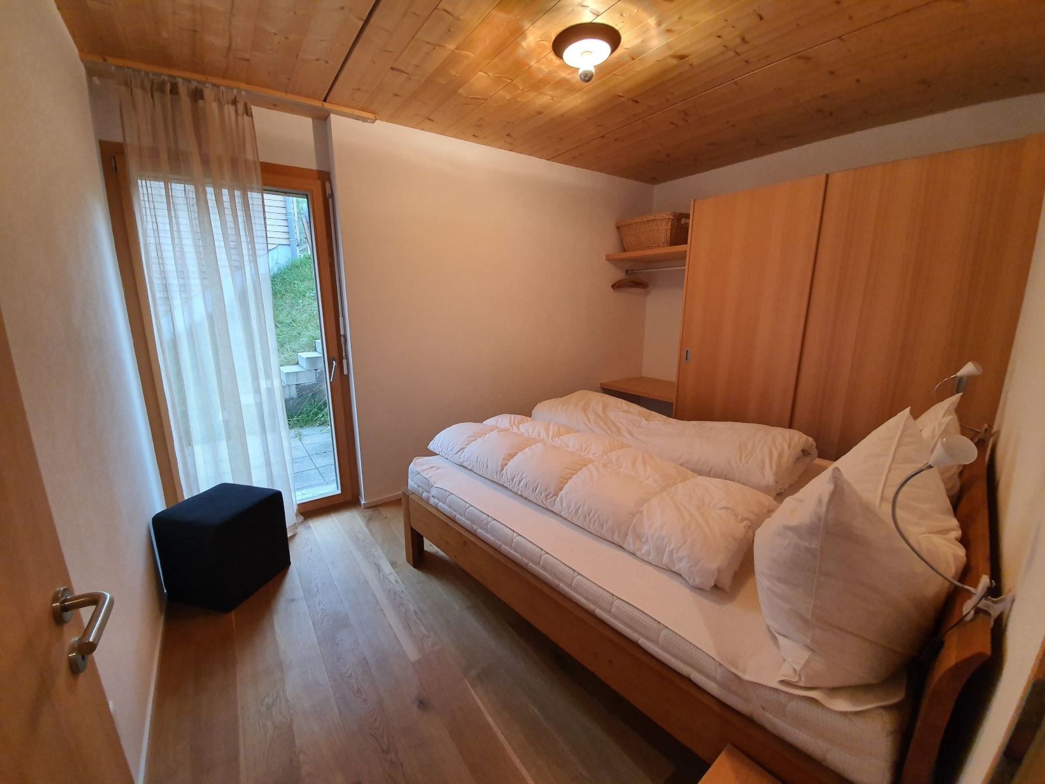 A bedroom with a wooden bed, a bench, a wardrobe, and a window with curtains.