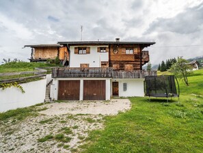 Ein zweigeschossiges Holzhaus mit Balkon, Trampolin und einem Schotterweg.