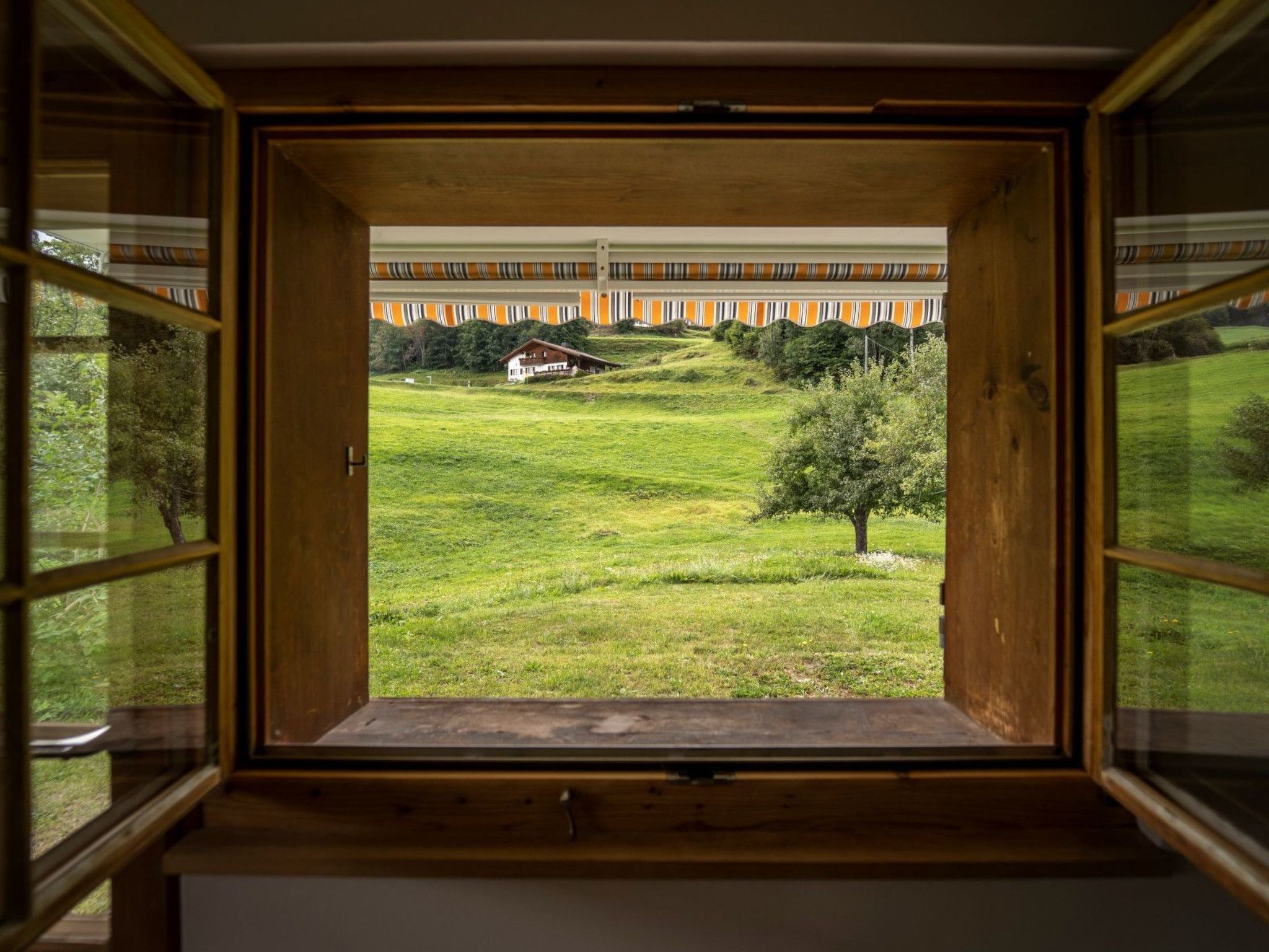 Ein Fenster mit Blick auf ein Wiesenfeld und ein Gebäude in der Ferne.
