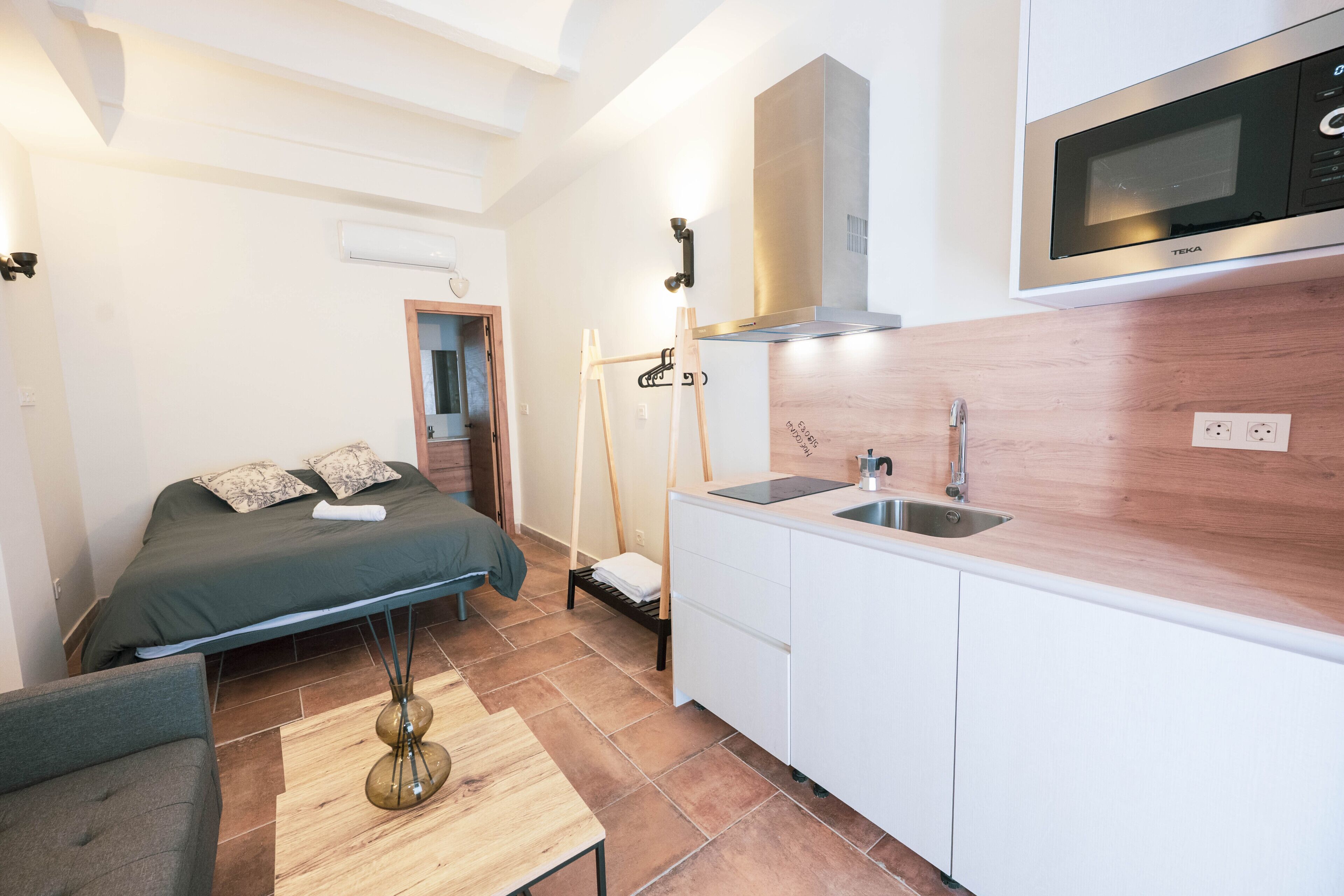 Une pièce de taille modeste comprenant un lit, un petit canapé, une table en bois, une kitchenette équipée d’un four à micro-ondes et un évier.