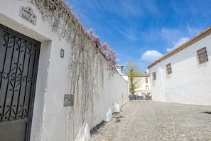 Une rue pavée, des bâtiments blancs, un portail en fer forgé et un ciel d’un bleu limpide.