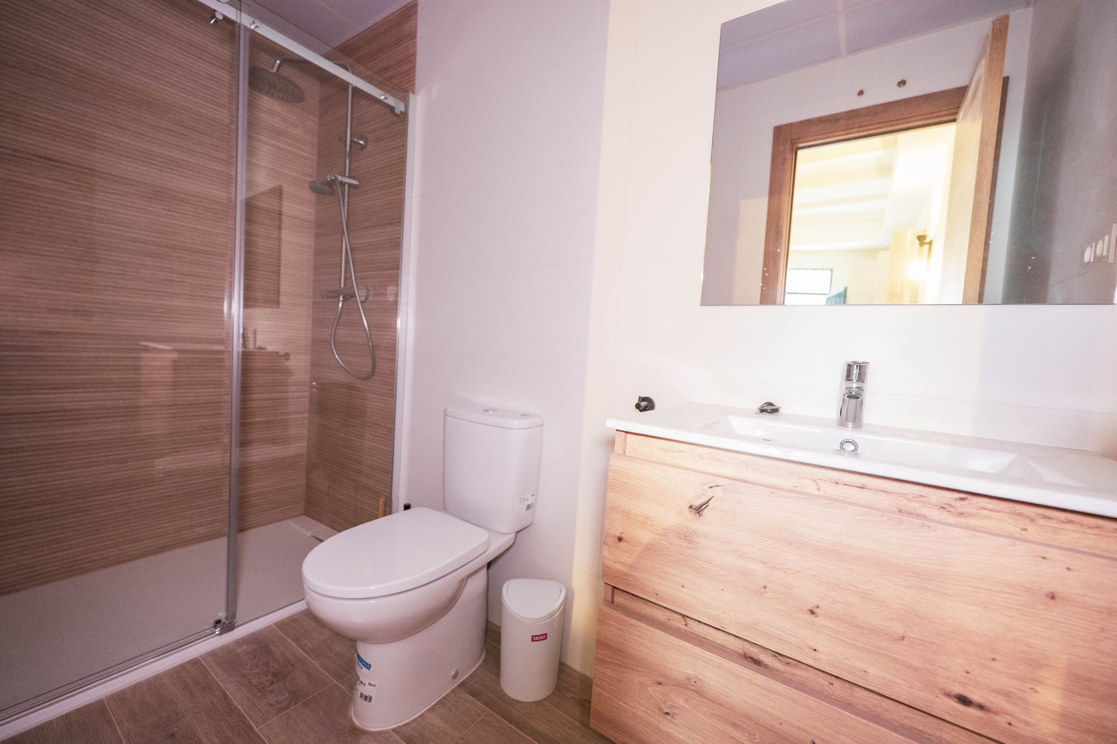 Une salle de bain avec une douche à parois de verre, des toilettes, un lavabo avec un meuble-vasque en bois et un miroir au-dessus du meuble-vasque.