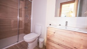 A bathroom with a glass shower enclosure, a toilet, a sink with a wooden vanity, and a mirror above the vanity.