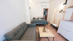 A compact room with a sofa, a small table, a bed, a dresser, and a door leading to another room.
