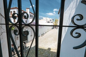 Blick durch ein Metallgitter auf eine Kopfsteinpflasterstraße, weiße Häuser und einen klaren Himmel.