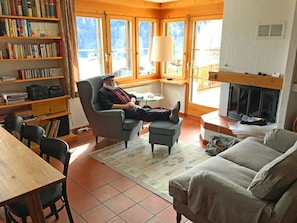 A cozy living room with a fireplace, a comfortable armchair, a sofa, and a bookshelf filled with books. - Crest Grond Herter, Waltensburg, (Waltensburg/Vuorz), 58006B by Interhome (Vuorz)