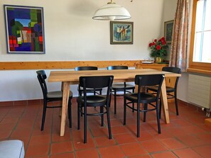 A dining area with a wooden table and black chairs, a painting on the wall, and a window with curtains. - Crest Grond Herter, Waltensburg, (Waltensburg/Vuorz), 58006B by Interhome (Vuorz)