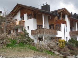 A multi-story building with balconies, a wooden facade, and a stone pathway leading to the entrance. - Crest Grond Herter, Waltensburg, (Waltensburg/Vuorz), 58006B by Interhome (Vuorz)