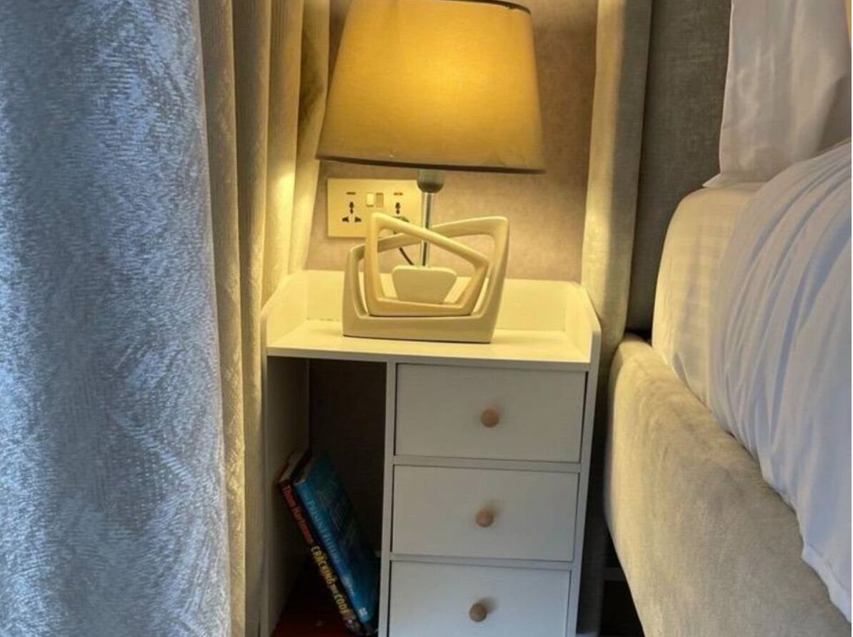 A bedside table with a lamp, a power outlet, and a drawer.