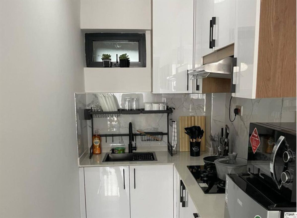 A modern kitchen with white cabinets, a black countertop, a built-in oven, and a window above the sink.