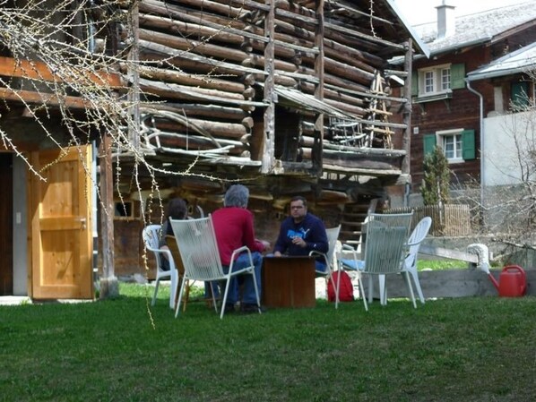 A rustic wooden building with a porch, outdoor seating, and a small table.