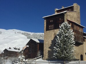 A snow-covered mountain scene with a wooden building and a snow-laden tree.