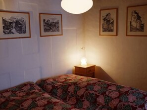 A bedroom with two beds, a bedside table with a lamp, and four framed pictures on the wall.