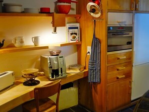 A kitchen with a coffee maker, a toaster, a kettle, and a refrigerator.