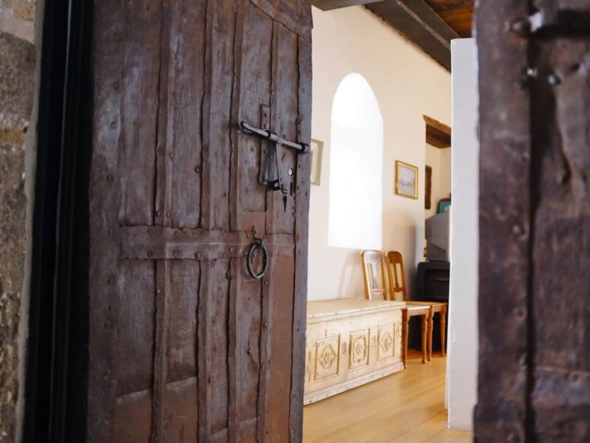 Uma porta de madeira rústica com puxador de metal, dando acesso a um quarto com soalho de madeira e um armário com padrão.