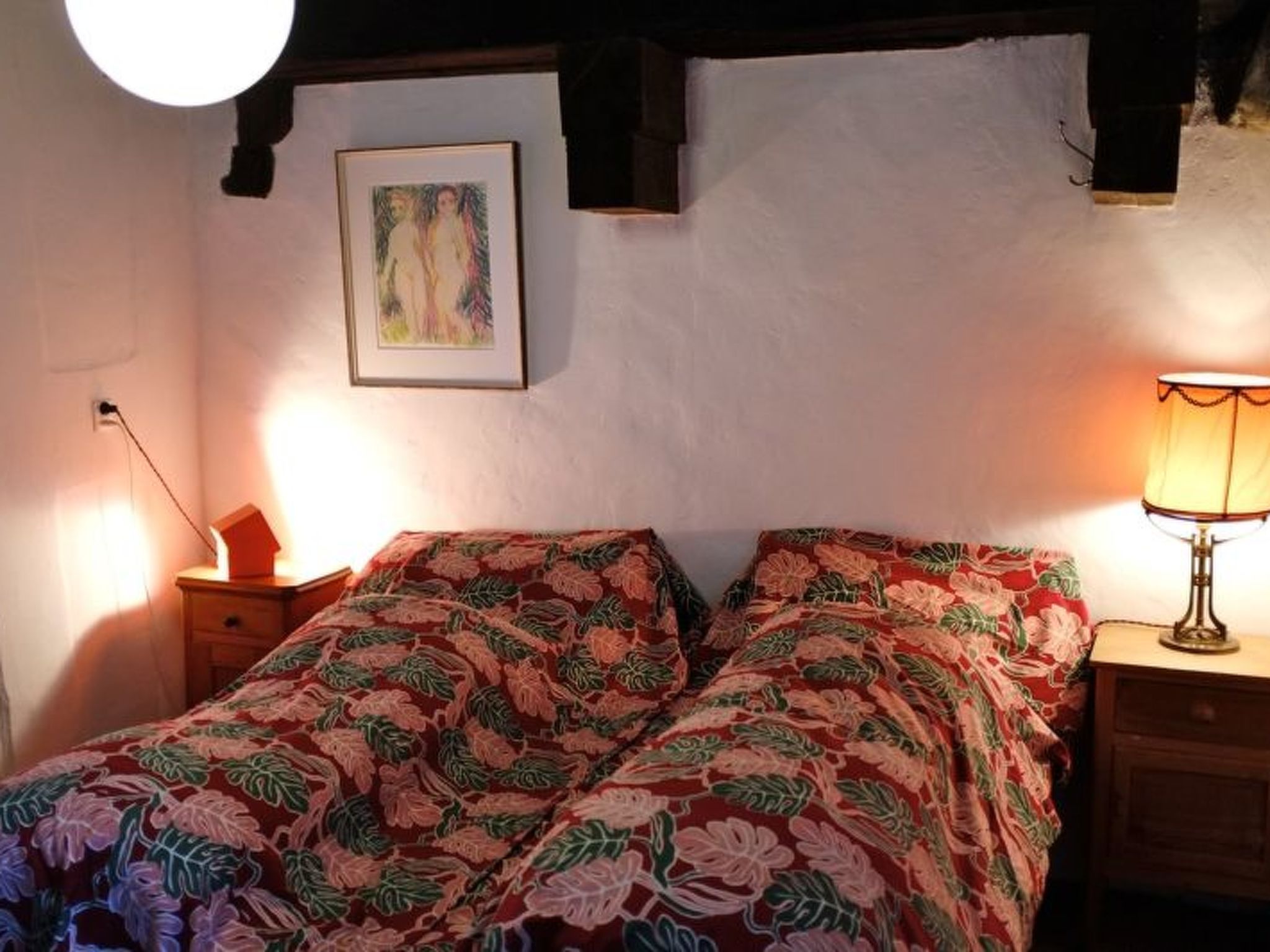 A bedroom with a bed, a nightstand, a lamp, and a painting on the wall.