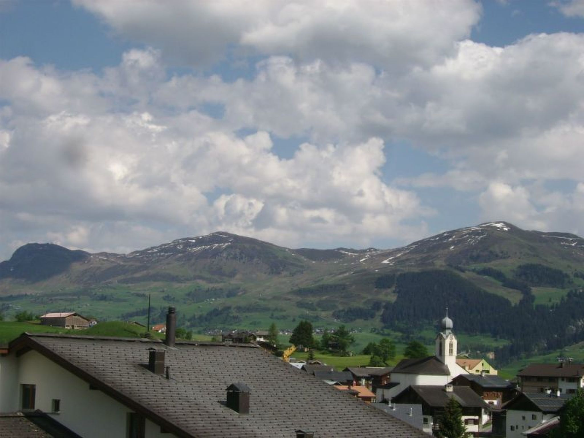 Eine gebirgige Landschaft mit einer Kirche und Wohnhäusern.