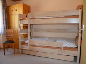 A bunk bed with a wooden frame, a chair, and a wardrobe in a room with a plain wall and carpeted floor. - Gabriela 25 Defuns, Brigels, (Breil/Brigels), 65050B by Interhome (Breil/Brigels)