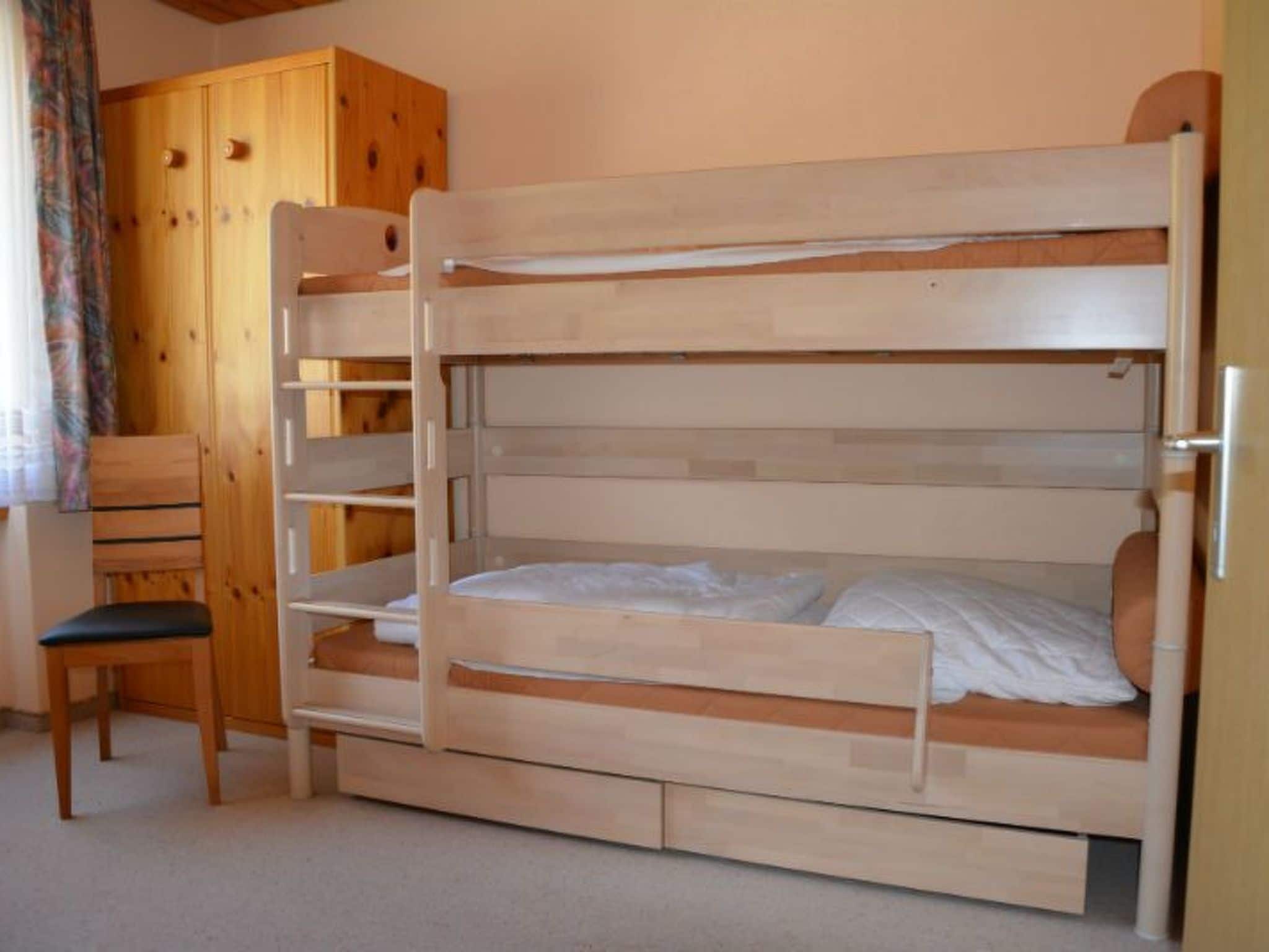 Una cama litera con estructura de madera y una silla.