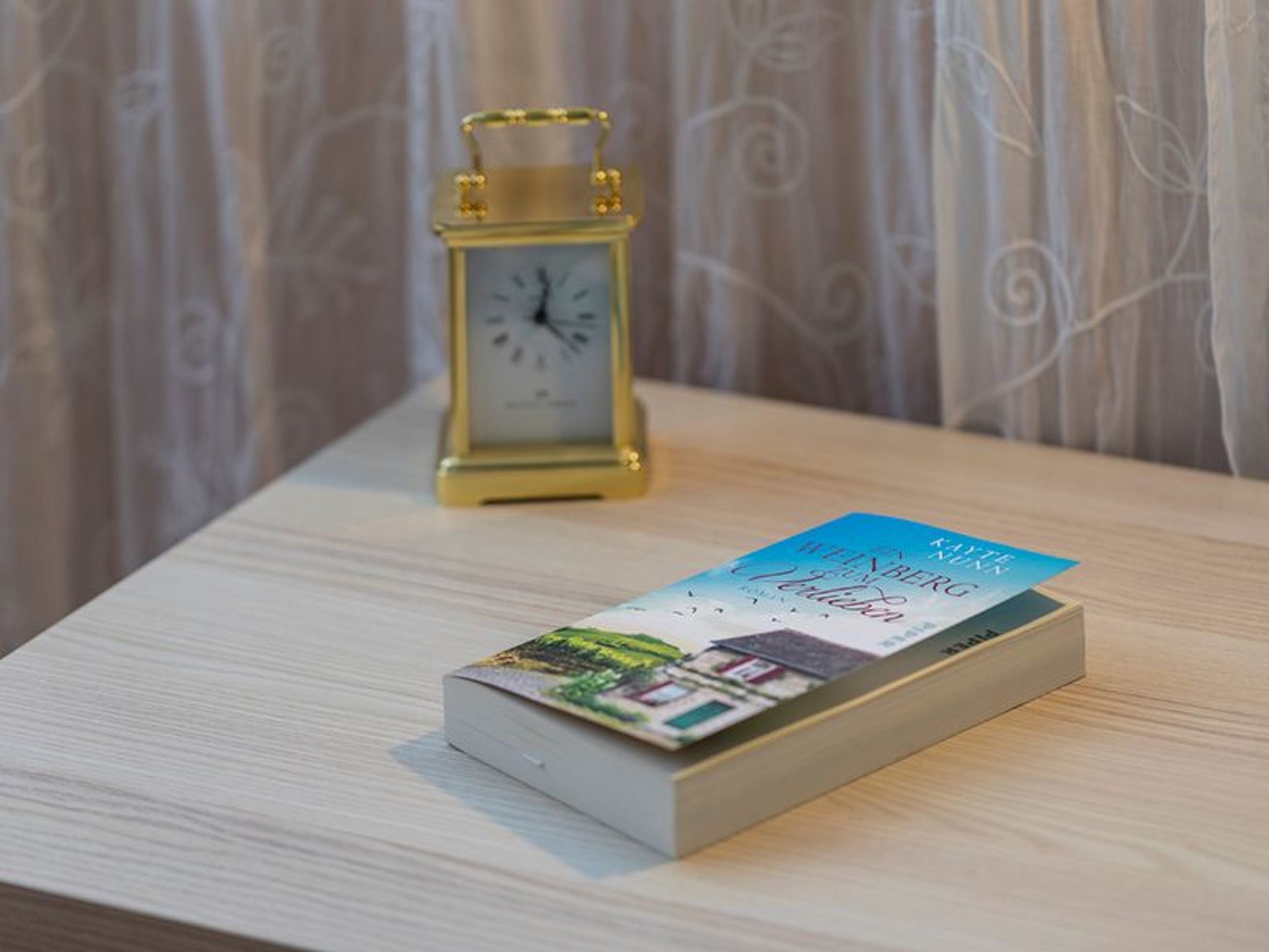 Un libro titulado 'Katten i Vinterberg' sobre una superficie de madera, con un reloj dorado al fondo.
