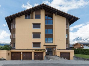 Un hotel a più piani con tetto piatto, ampie finestre e uno sfondo montuoso.
