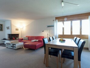 Una sala moderna con un sofá rojo, una mesa de comedor con sillas, una chimenea y ventanas grandes.