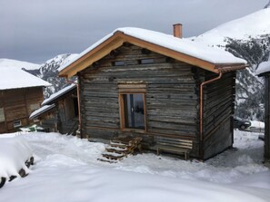 Una cabaña de madera con techo inclinado y chimenea, rodeada de montañas nevadas.